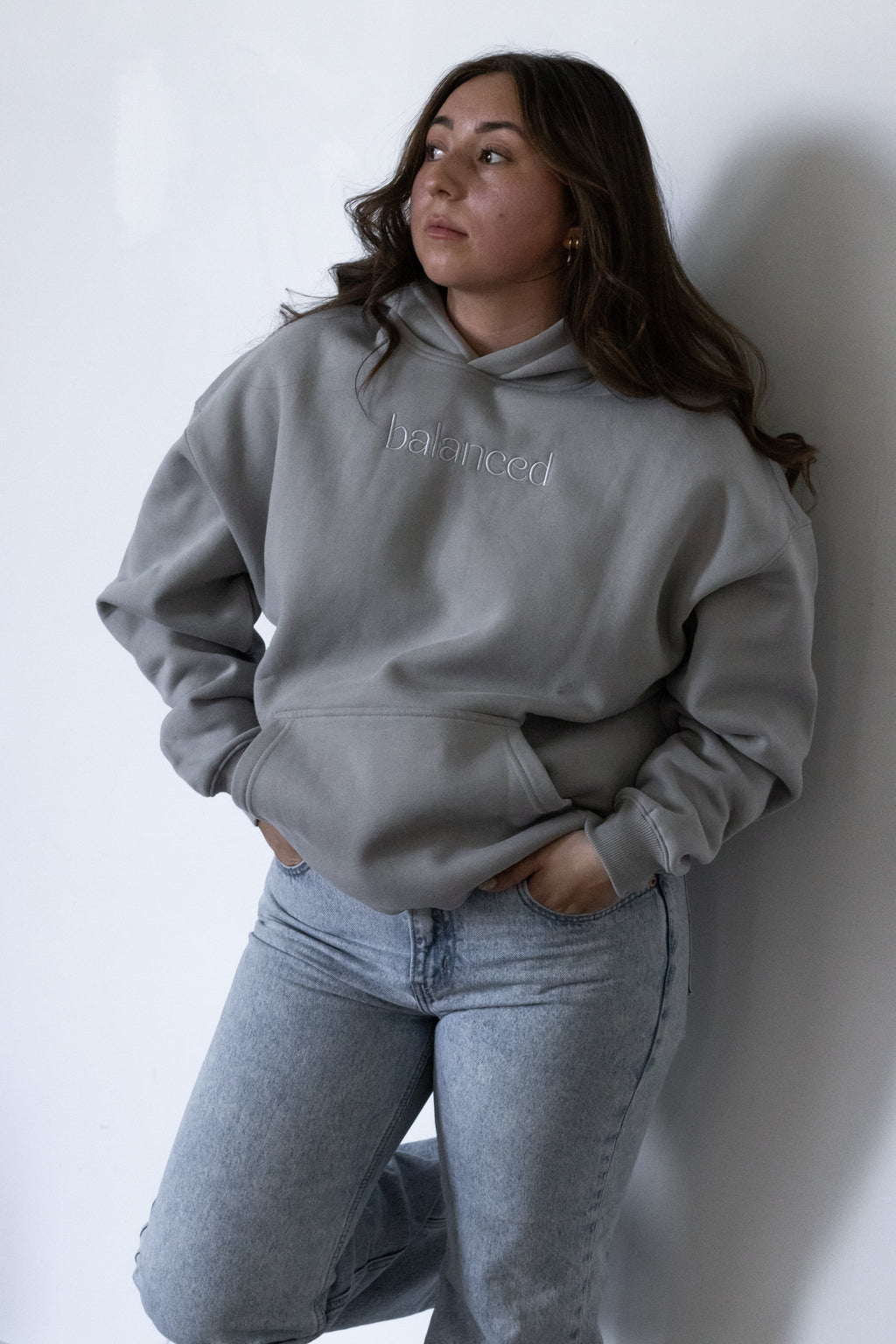 Person wearing a gray hoodie with text and jeans against a white wall