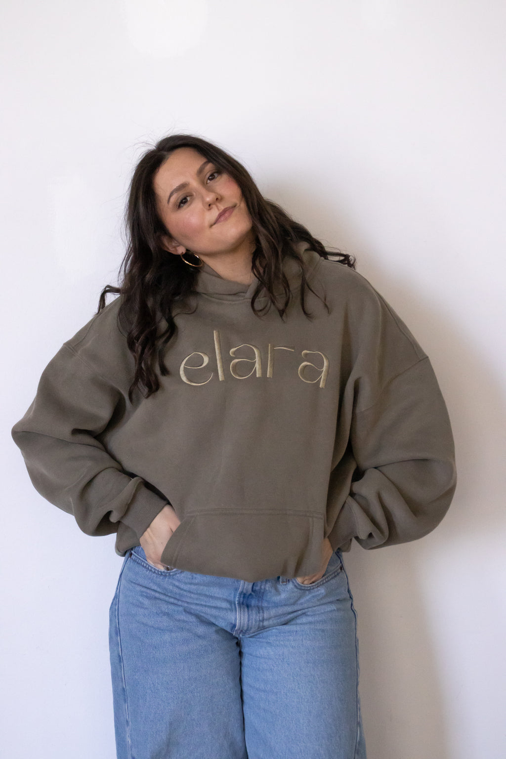 Woman wearing a gray sweatshirt with 'elara' printed on it against a white background