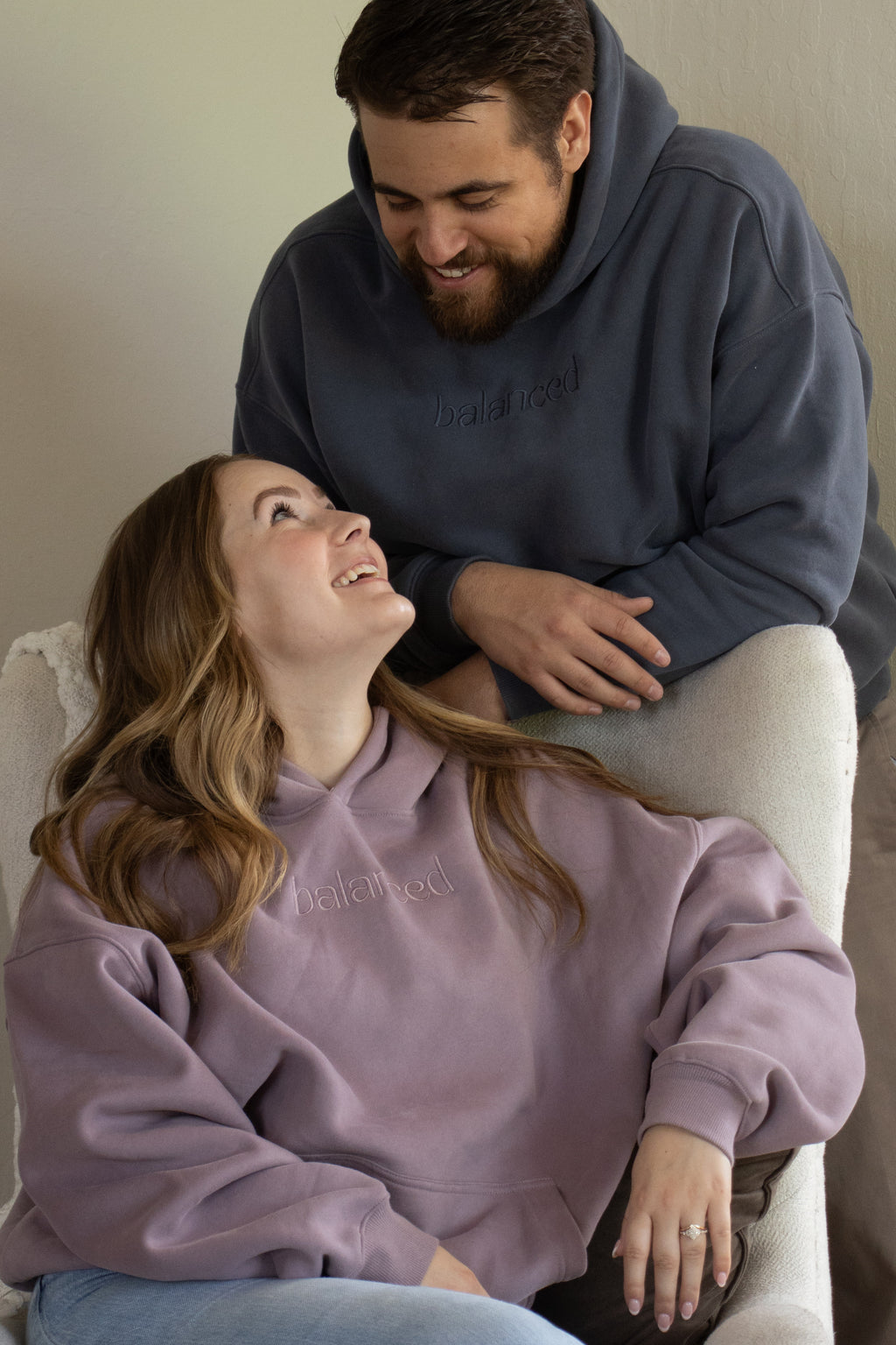 Two people wearing matching hoodies, one in purple and the other in dark blue, sitting on a couch.