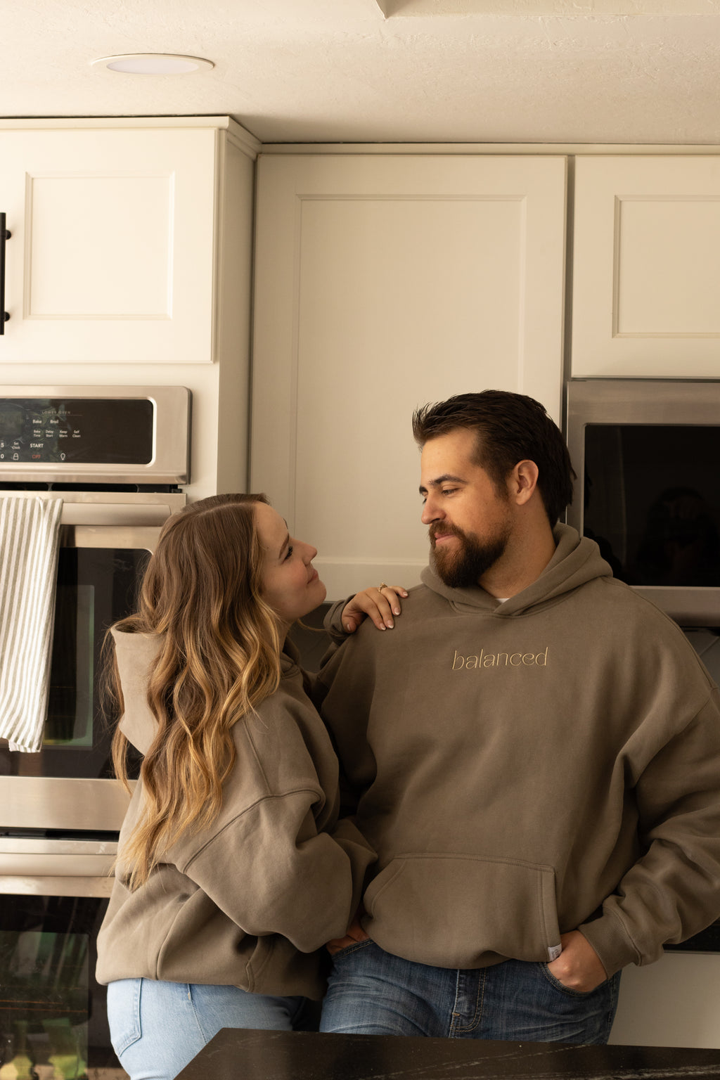 Man and woman standing in a kitchen, both wearing hoodies.