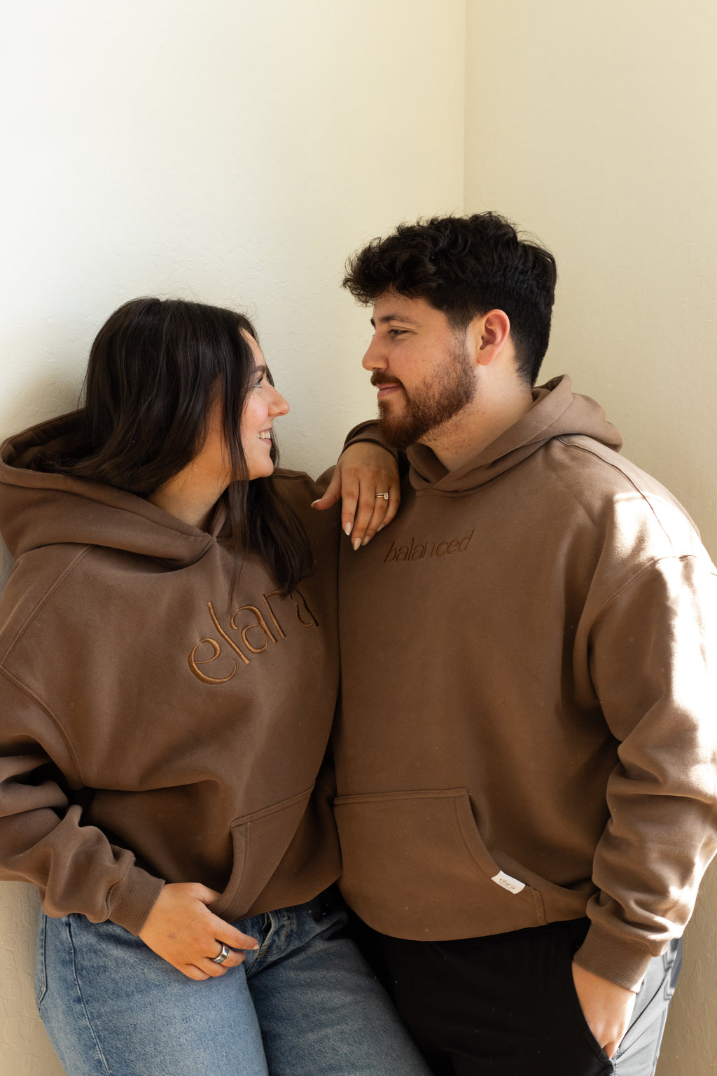 Two people wearing brown hoodies against a plain background