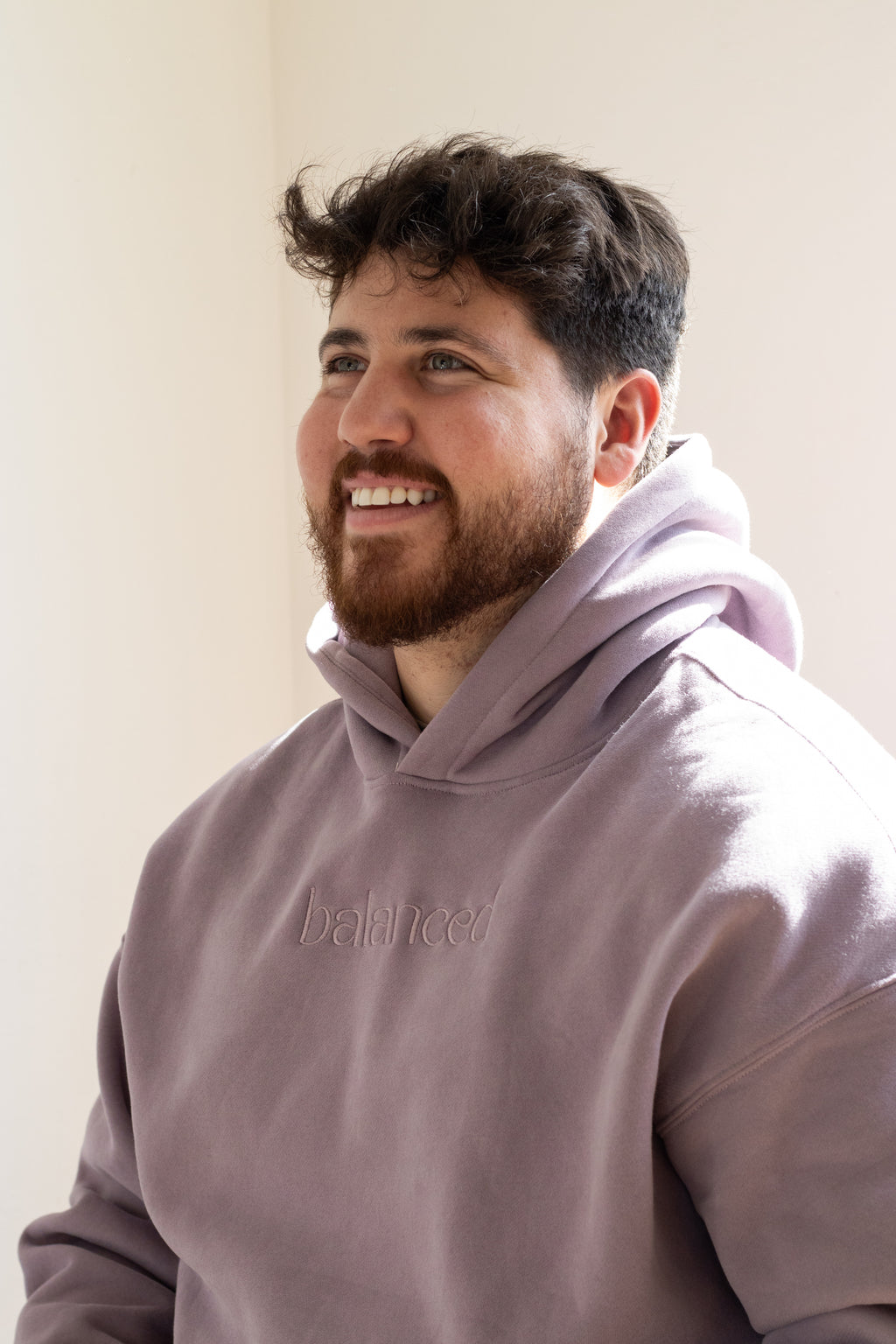 Man wearing a light purple hoodie with 'balanced' text against a plain background